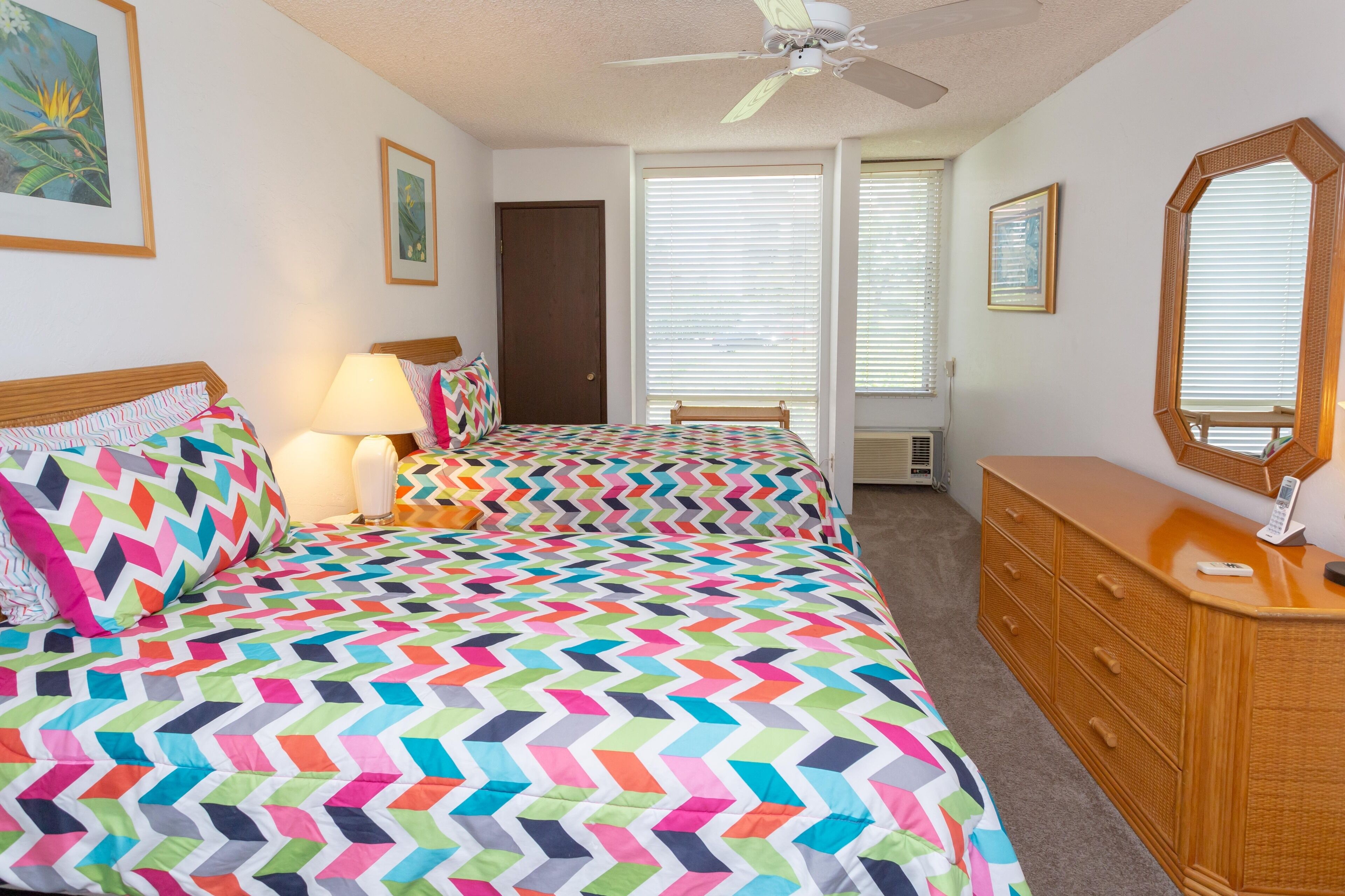 Une chambre avec deux lits, une commode, un ventilateur de plafond et un grand miroir.