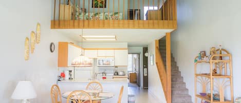 Un vaste espace de vie comprenant une table à manger, des chaises, un ventilateur de plafond et un escalier menant à l’étage supérieur.