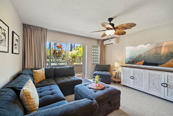 A modern living room with a sectional sofa, ottoman, and a flat-screen TV.