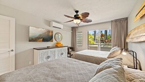 A bedroom with two beds, a ceiling fan, a painting, a dresser, and a window with curtains.