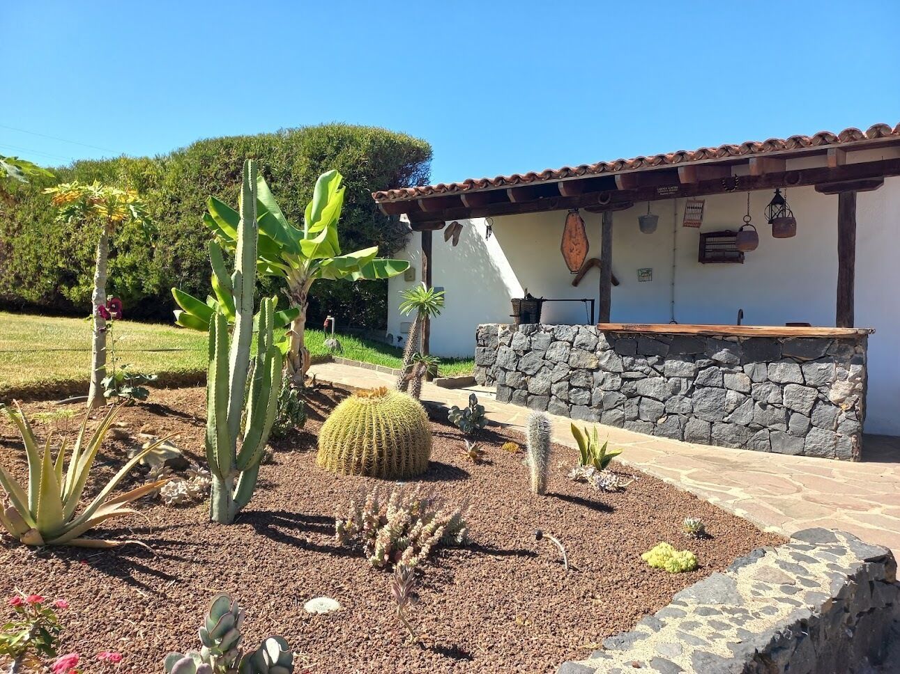 A building with a stone wall and a tiled roof, surrounded by a garden with various cacti and succulents.