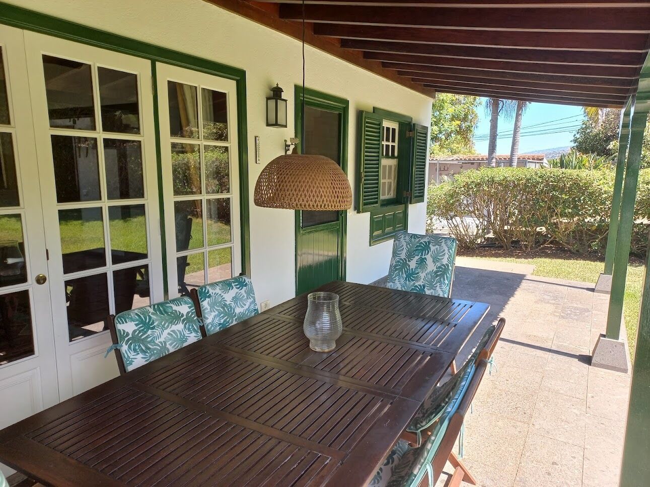 Een houten tafel met stoelen, een hanglamp en uitzicht op een tuin.