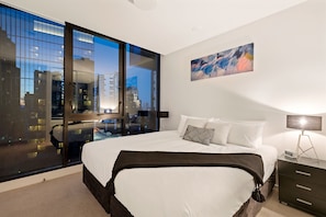 A modern hotel room with a large bed, a city view through floor-to-ceiling windows, a painting on the wall, and a bedside table with a lamp. - Premier Stays Melbourne (Southbank)