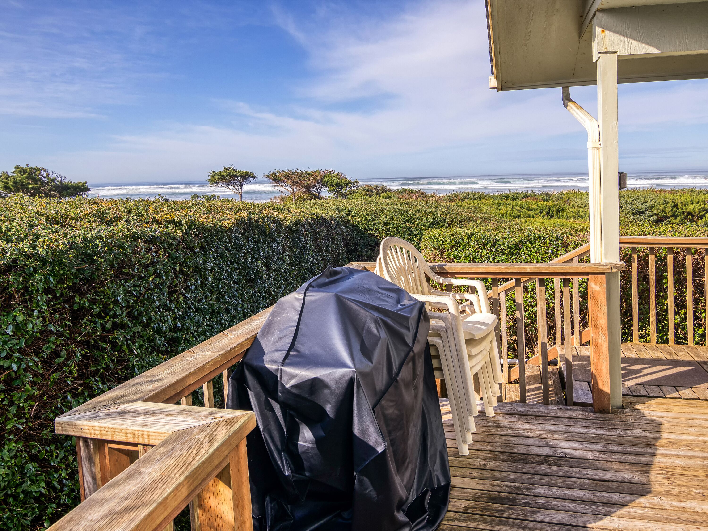 Eine Holzterrasse mit überdachtem Grill, einem Stuhl und einem Tisch mit Blick auf den Ozean.