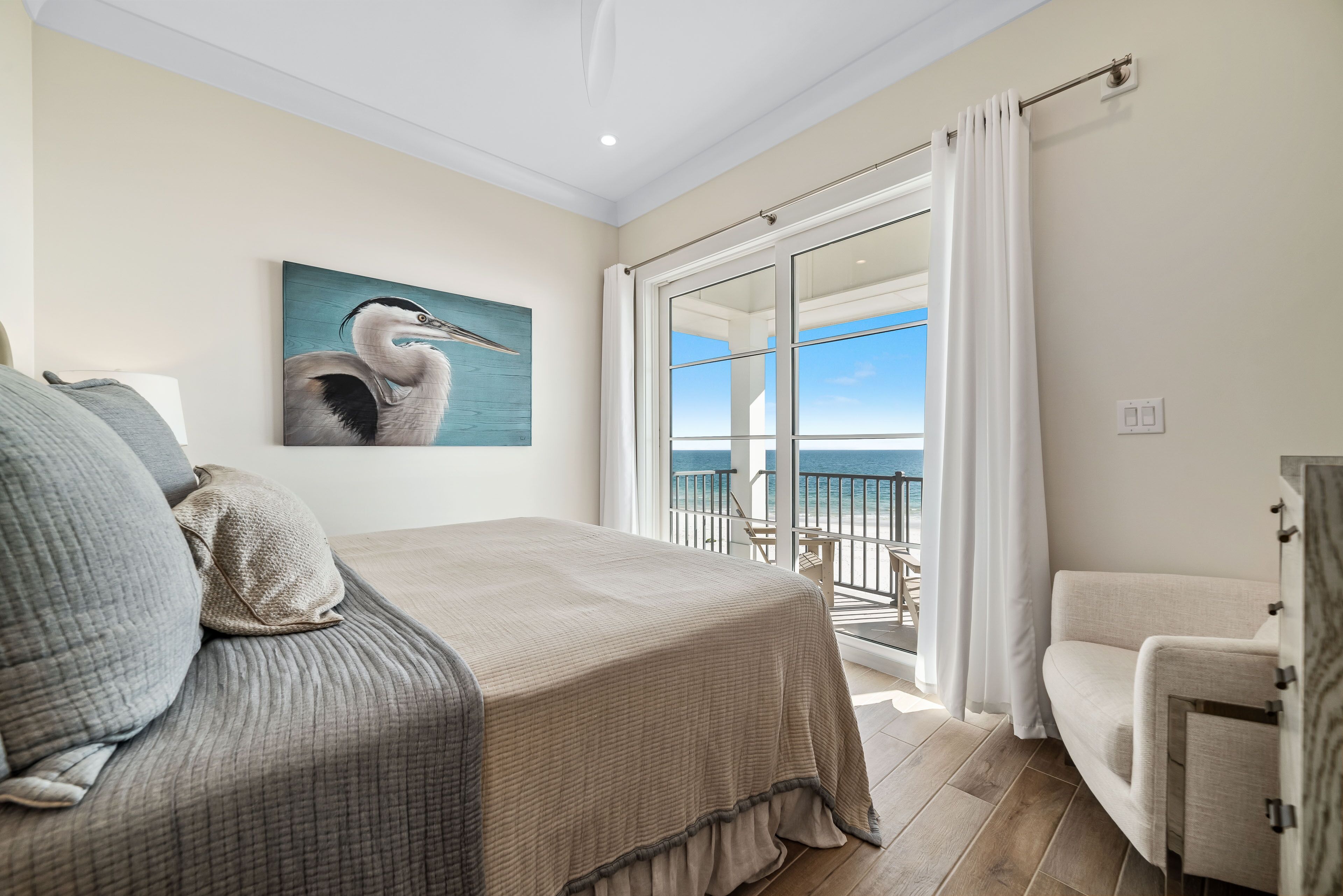Une chambre avec un lit, un tableau, un balcon donnant sur la mer et une chaise.