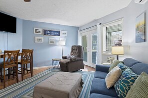 Una sala de estar con pared azul, televisor, silla, sofá y ventana con persianas.