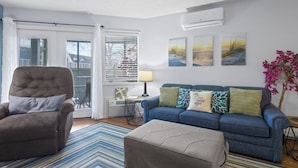 A living room with a blue sofa, a brown armchair, a small table with a lamp, and a window with blinds.
