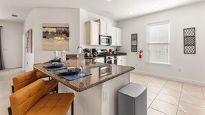 Een moderne keuken met witte kastjes, een granieten aanrechtblad en een eethoek met oranje stoelen.
