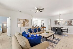 A spacious living room with a beige sofa, blue cushions, a coffee table, and a ceiling fan.