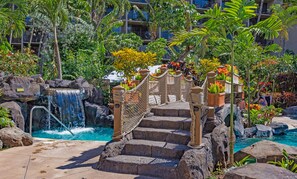 A pool area with a waterfall, stone steps, and tropical plants.