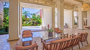 Um hall amplo com uma mesa de centro de vidro, cadeiras de vime e vista para um jardim tropical.