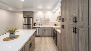 A modern kitchen with wooden cabinets, stainless steel appliances, and a white countertop. - STUNNING BRAND NEW REMODEL-OCEAN VIEWS-LARGE LANAI-AC-WELL EQUIPPED (Kihei)