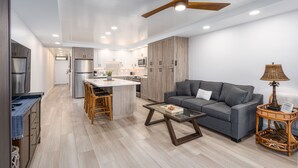 A modern kitchen with wooden cabinets, a central island, and a dining area with chairs. - STUNNING BRAND NEW REMODEL-OCEAN VIEWS-LARGE LANAI-AC-WELL EQUIPPED (Kihei)