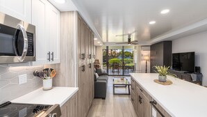 A modern kitchen with a built-in microwave, stove, and oven. It features light wood cabinetry, a white countertop, and a view of a patio with outdoor furniture. - STUNNING BRAND NEW REMODEL-OCEAN VIEWS-LARGE LANAI-AC-WELL EQUIPPED (Kihei)
