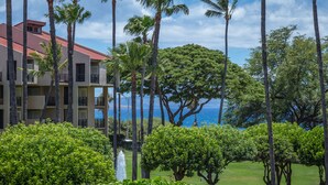 A hotel with a red roof, multiple balconies, and lush greenery including palm trees and bushes. - STUNNING BRAND NEW REMODEL-OCEAN VIEWS-LARGE LANAI-AC-WELL EQUIPPED (Kihei)