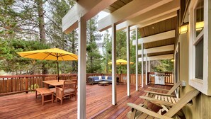 Una terraza de madera con mobiliario exterior, incluyendo una mesa y sillas, y dos sombrillas amarillas.