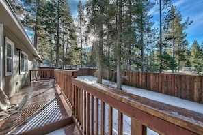 Une terrasse en bois avec une rambarde, entourée d’arbres et d’un sol recouvert de neige.