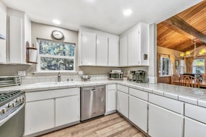Una cocina moderna con armarios blancos, lavavajillas de acero inoxidable y techo de madera.