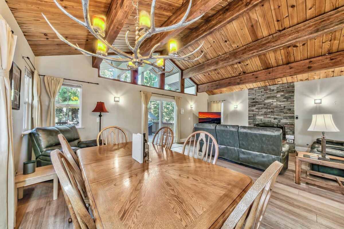 A spacious dining area with a wooden table and chairs, a chandelier, and a stone wall in the background.