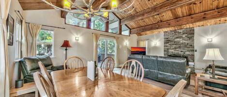 A spacious dining area with a wooden table and chairs, a chandelier, and a stone wall in the background.
