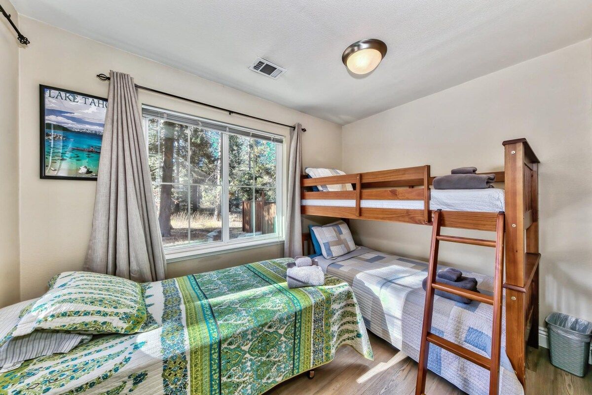 A room with a bunk bed, a window with curtains, a framed picture, and a ladder.
