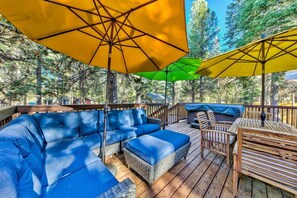 Eine Holzterrasse mit Gartenmöbeln, darunter ein blaues Sofa und Stühle, sowie zwei große Sonnenschirme, die Schatten spenden.