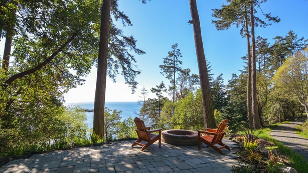 En uteplats med två trästolar i Adirondack-stil, en rund eldstad och utsikt över havet.