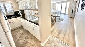 A modern kitchen with white cabinets and a black countertop, a dining area with a round table and chairs, and a large window providing natural light. - Amazing 14th floor views! Perfect for Couples! 4344BS2 (Miramar Beach)