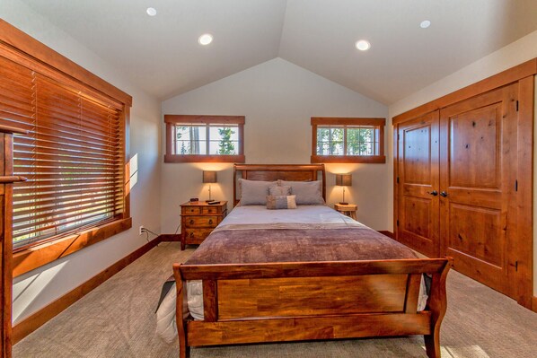 A bedroom with a wooden bed, two bedside tables with lamps, a large wardrobe, and a sloped ceiling with recessed lighting.