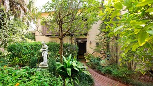Un sentier de jardin menant à un bâtiment orné d’une statue et entouré d’une végétation luxuriante.