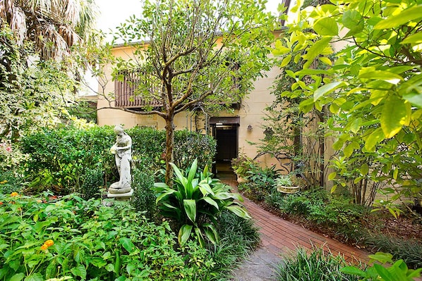Um caminho no jardim leva a um edifício com uma estátua e vegetação exuberante.