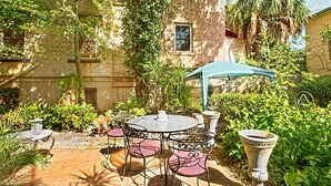 Une cour avec une table ronde et des chaises, entourée d’une végétation luxuriante et d’un bâtiment recouvert de lierre.