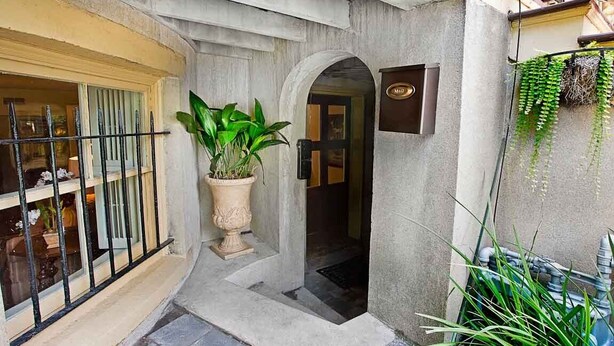 Une entrée d’immeuble avec un pot de fleurs, une petite arche et une enseigne au-dessus de la porte.