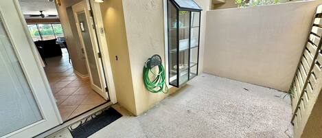 A balcony with a sliding glass door, a green garden hose, and a metal shelf.