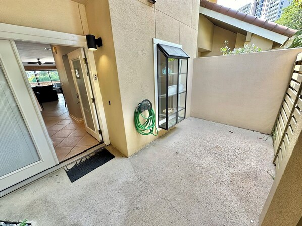 A balcony with a sliding glass door, a green garden hose, and a metal shelf.