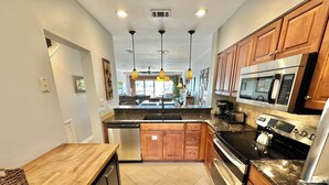A modern kitchen with granite countertops, wooden cabinets, stainless steel appliances, and pendant lighting. - Fresh updates with Golf Cart! 5197 BW (Miramar Beach)