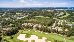 An aerial view of a golf course with sand bunkers, surrounded by residential areas and a distant city skyline. - Fresh updates with Golf Cart! 5197 BW (Miramar Beach)