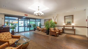 A lobby with a reception desk, wicker chairs, a glass coffee table, potted plants, a console table with lamps, and a large mirror. - Ocean view studio with washer/dryer, FREE parking & Wi-Fi! (Honolulu)