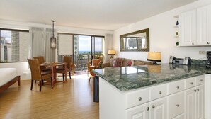 A hotel room with a balcony, a dining area, a kitchen, and a large bed. - Ocean view studio with washer/dryer, FREE parking & Wi-Fi! (Honolulu)