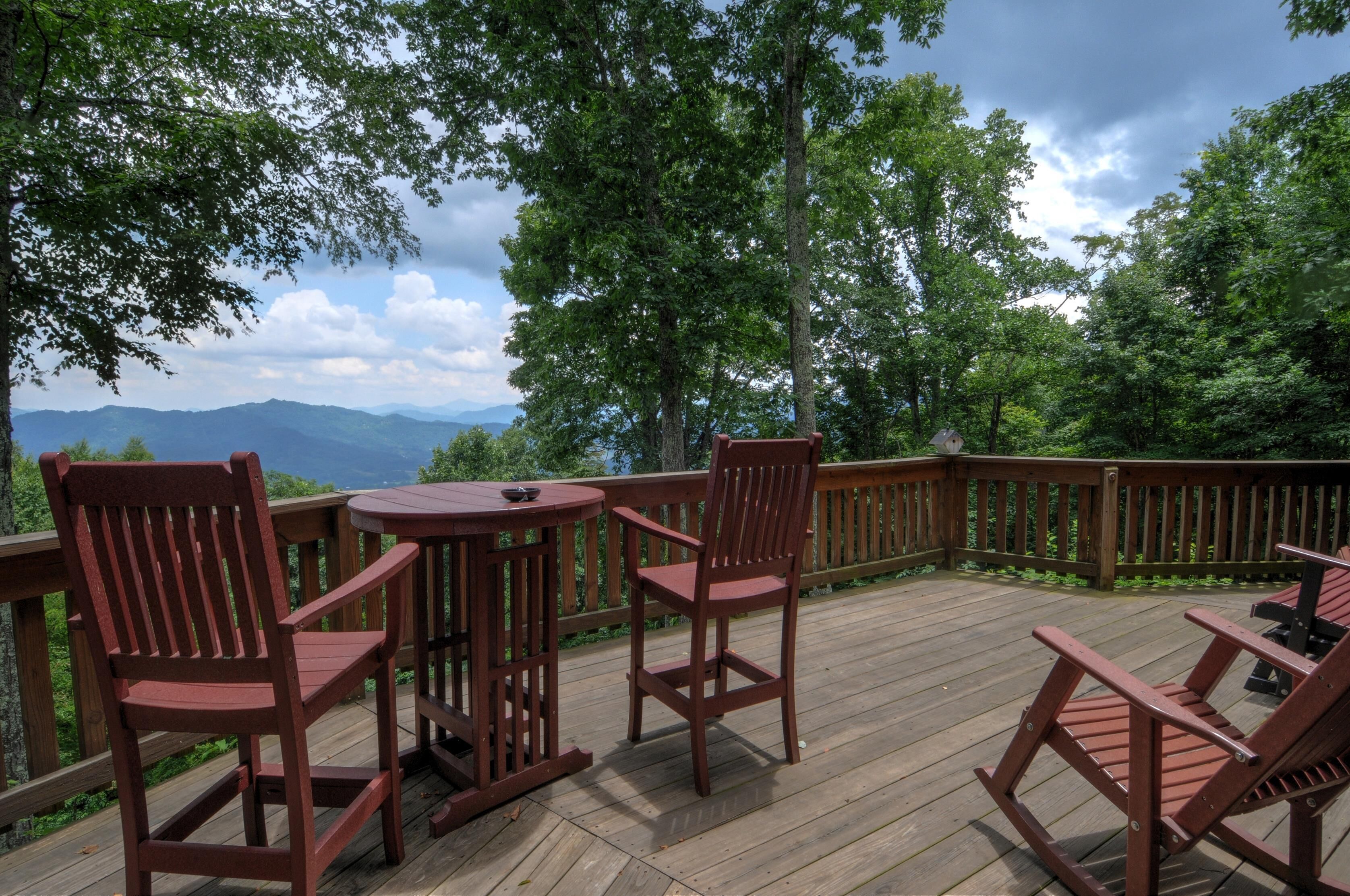 Eine Holzterrasse mit Tisch und Stühlen, umgeben von einem Holgitter, mit Blick auf eine Berglandschaft.