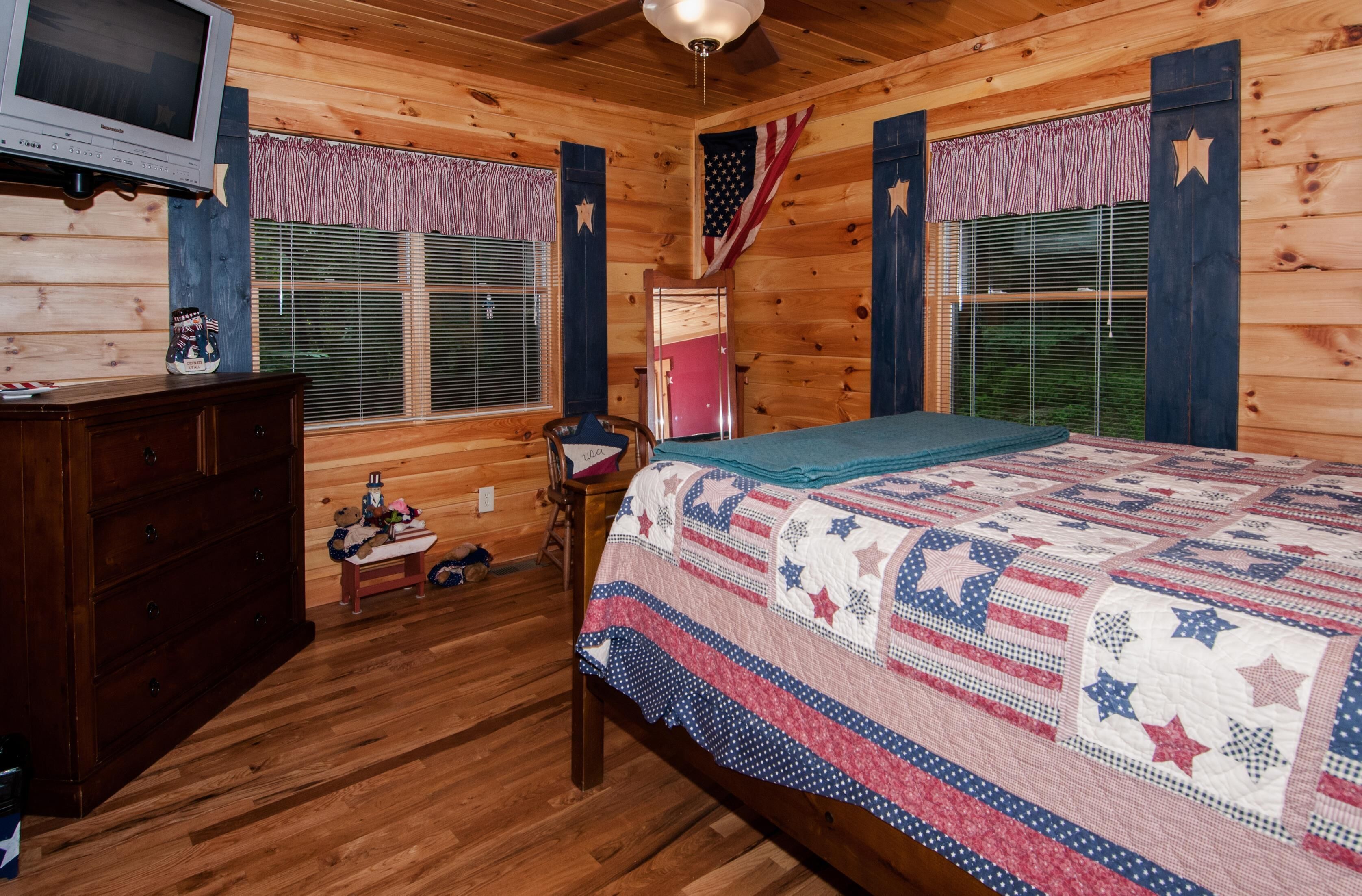 Ein Schlafzimmer einer Holzhütte mit Bett, Schminktisch, Fernseher und Dekorationen mit amerikanischer Flagge.