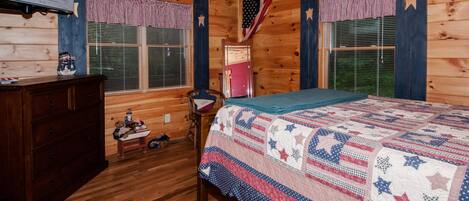 Ein Schlafzimmer einer Holzhütte mit Bett, Schminktisch, Fernseher und Dekorationen mit amerikanischer Flagge.