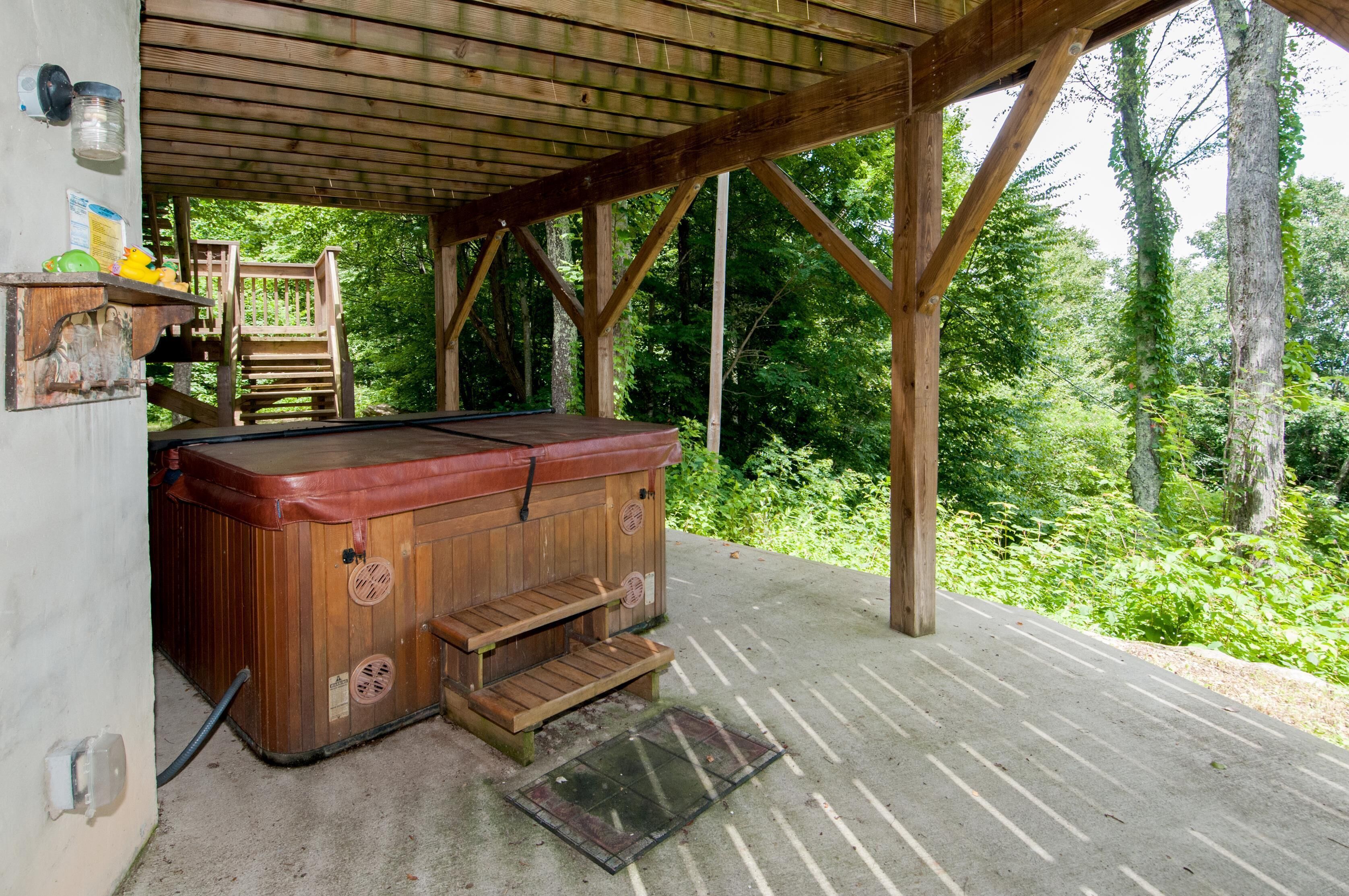 Un jacuzzi de madera bajo un porche cubierto con vistas a un bosque.