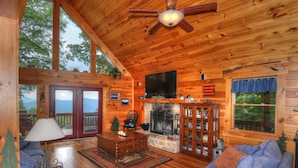 Een gezellig houten chalet interieur met een open haard, houten vloeren, een televisie en een groot raam met uitzicht op het landschap.