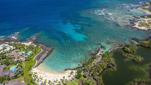 An aerial view of a coastal resort with clear turquoise waters, a sandy beach, and lush greenery. - Local Luxury Living! (Kamuela)