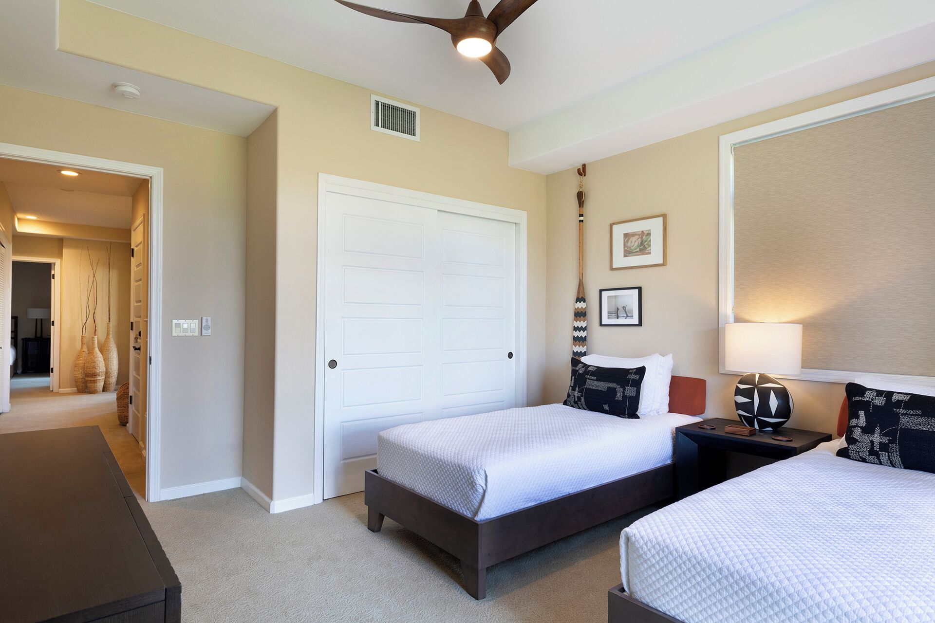 A hotel room with two beds, a ceiling fan, a large window, and a door leading to another room.