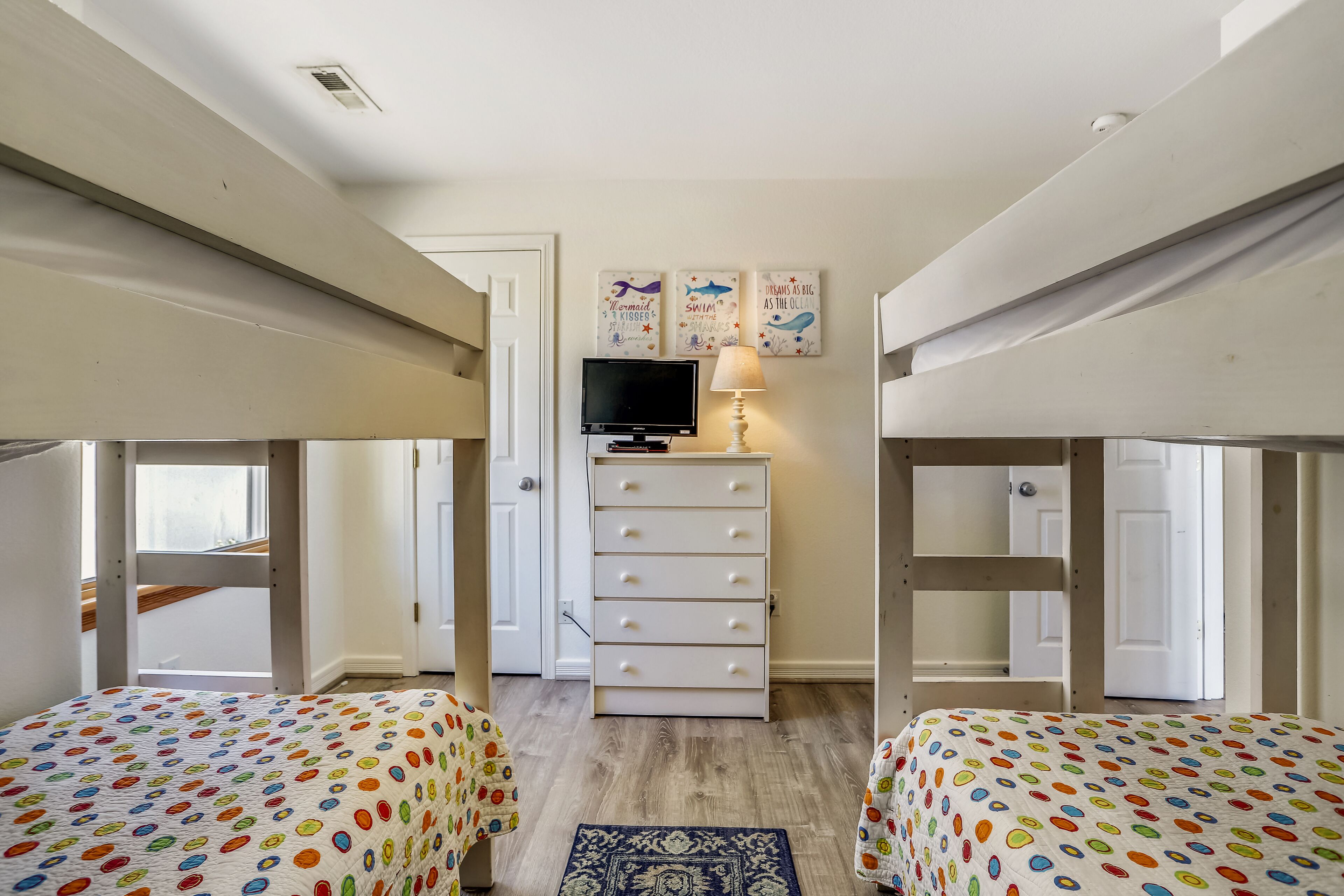 A room with bunk beds, a TV, a dresser, and wall art.