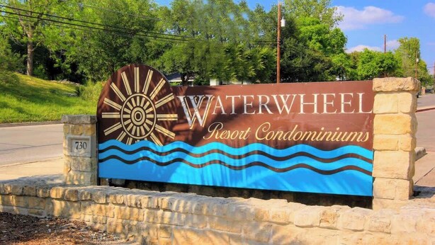 A sign for Waterwheel Resort Condominiums with a sun wheel design and wavy water graphic. - WW C302 Gracelanda (New Braunfels)