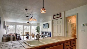 A kitchen with a large island, a ceiling fan, pendant lights, a dining area with chairs, and a view through large windows. - WW C302 Gracelanda (New Braunfels)