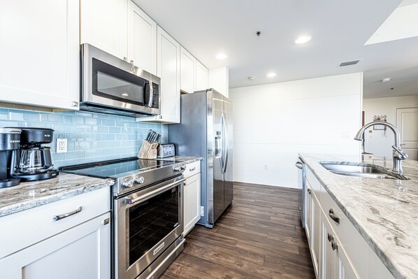 A modern kitchen with white cabinets, stainless steel appliances, a microwave, oven, and refrigerator.
